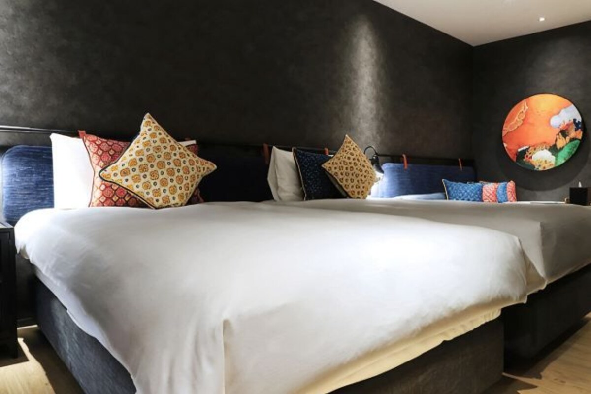 A bed with white bedding and multiple pillows, a dark wall, and a circular artwork on the wall.