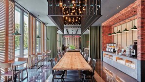 Uma ampla área de refeições com uma longa mesa de madeira, várias cadeiras e um espaço para café com diversos equipamentos.