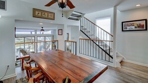 A spacious dining area with a wooden table and chairs, a ceiling fan, and a staircase with a railing. - Anchors Away - Hosted By Moore AI Rentals (Fernandina Beach)