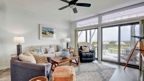 A spacious living room with a large window, a ceiling fan, and a view of the outdoors. - Anchors Away - Hosted By Moore AI Rentals (Fernandina Beach)