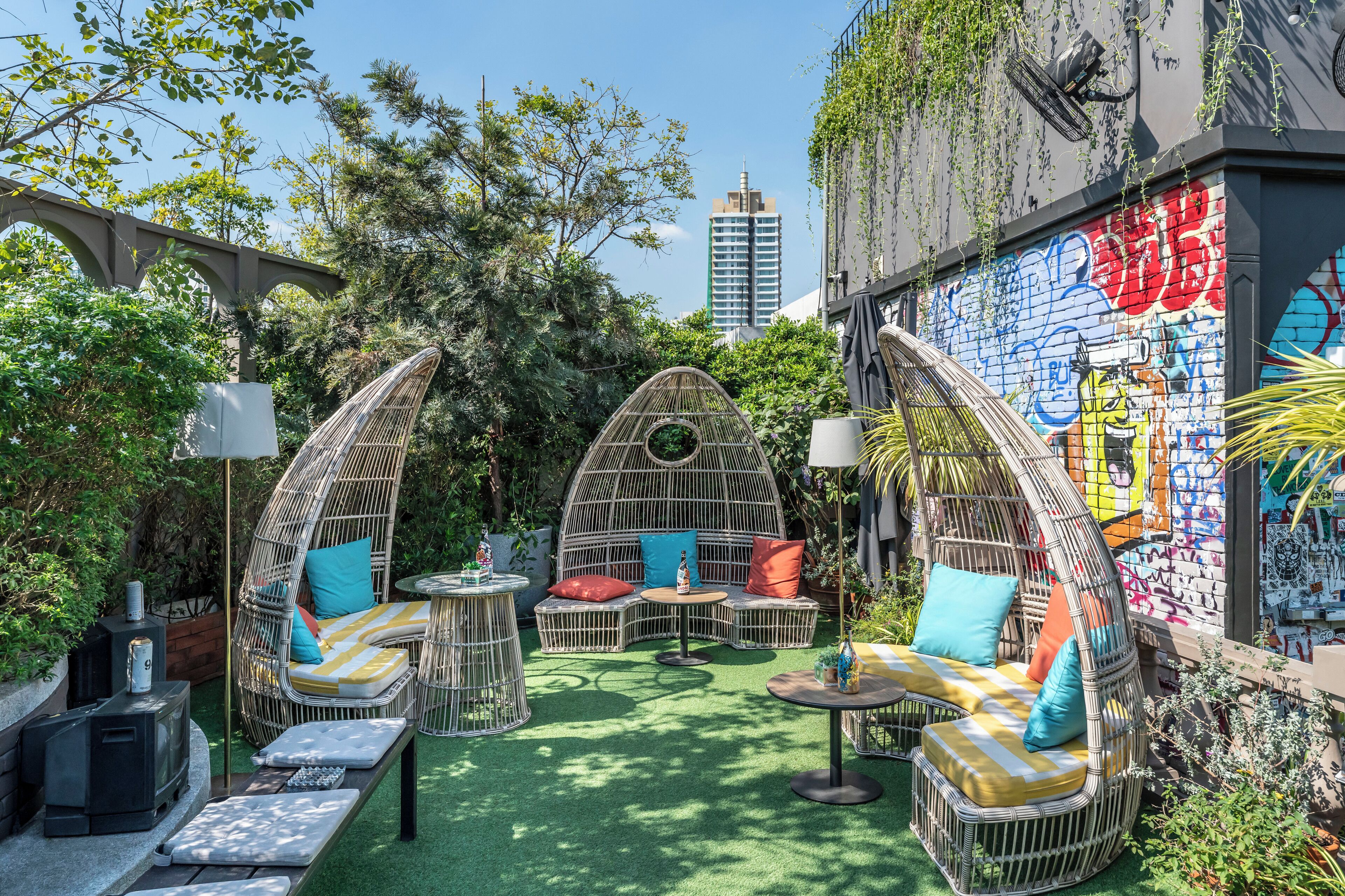 A rooftop garden with wicker furniture, a small grill, and a graffiti-covered wall.