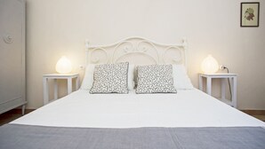 Una cama bien tendida con ropa blanca y dos almohadas estampadas, flanqueada por dos mesitas de noche con lámparas.