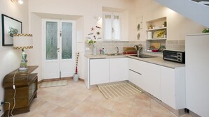 Una cocina con armarios blancos, un fregadero, un tostador y una ventana pequeña con adornos.