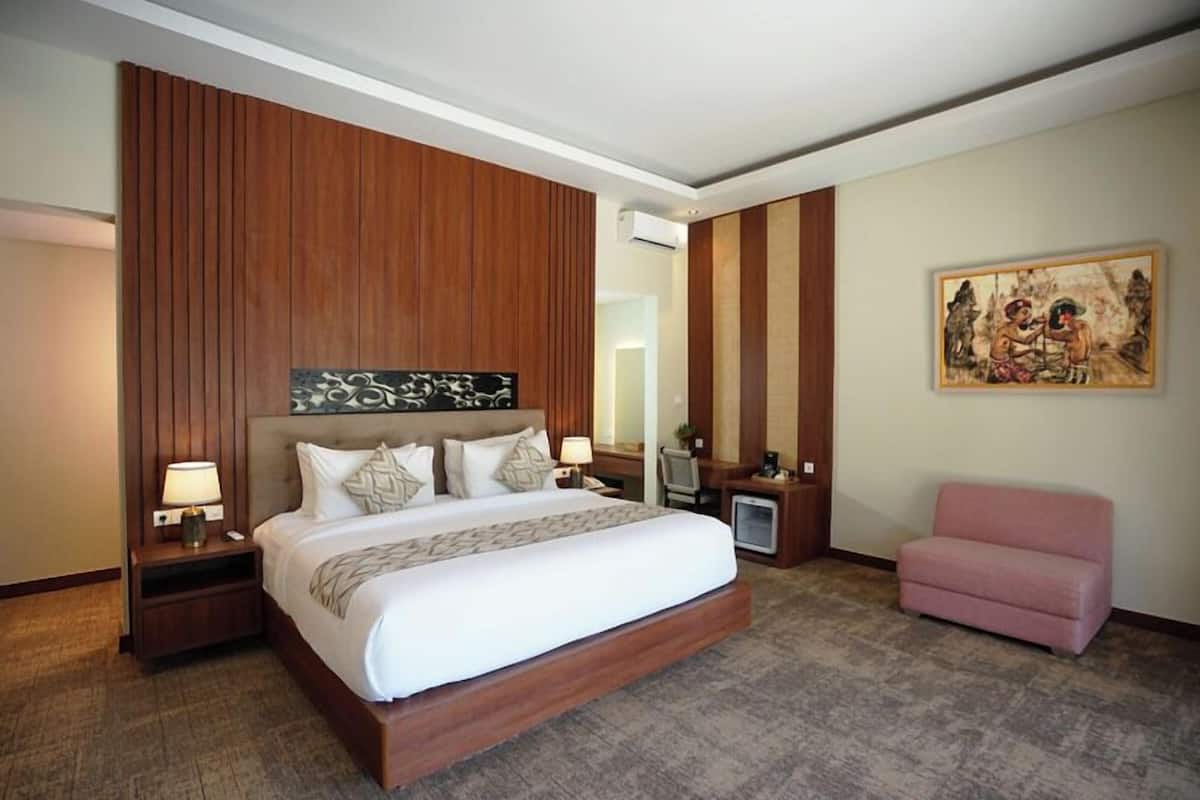Una habitación de hotel con una cama grande, paneles de madera, un televisor pequeño, un sillón rosa y un cuadro en la pared.