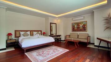A hotel room with a large bed, a sofa, a small table, a chair, a decorative mirror, and a painting on the wall.