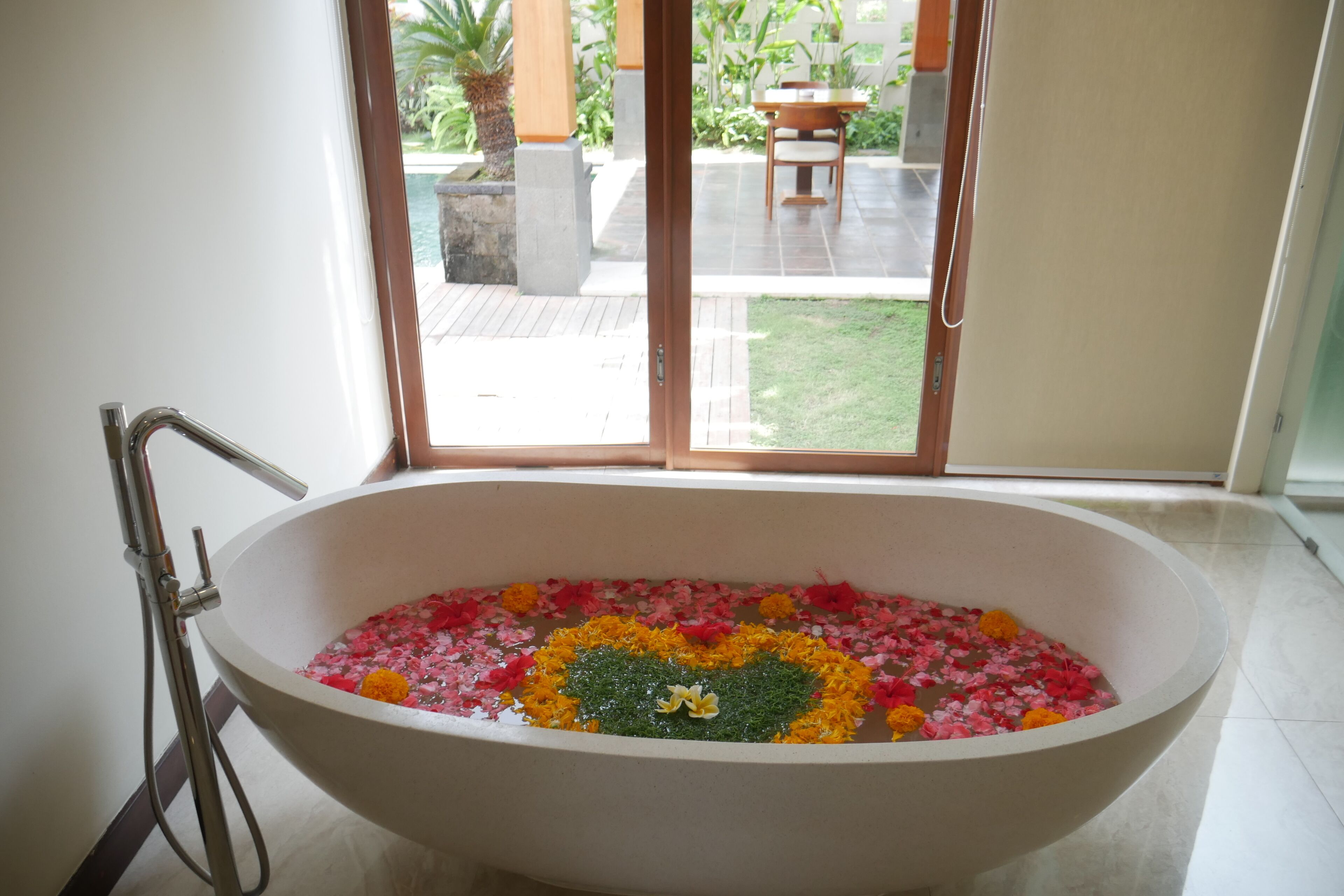 Una bañera llena de agua y pétalos de flores, con vistas a un patio y zona de estar al aire libre.