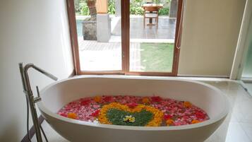 Una bañera llena de agua y pétalos de flores, con vistas a un patio y zona de estar al aire libre.