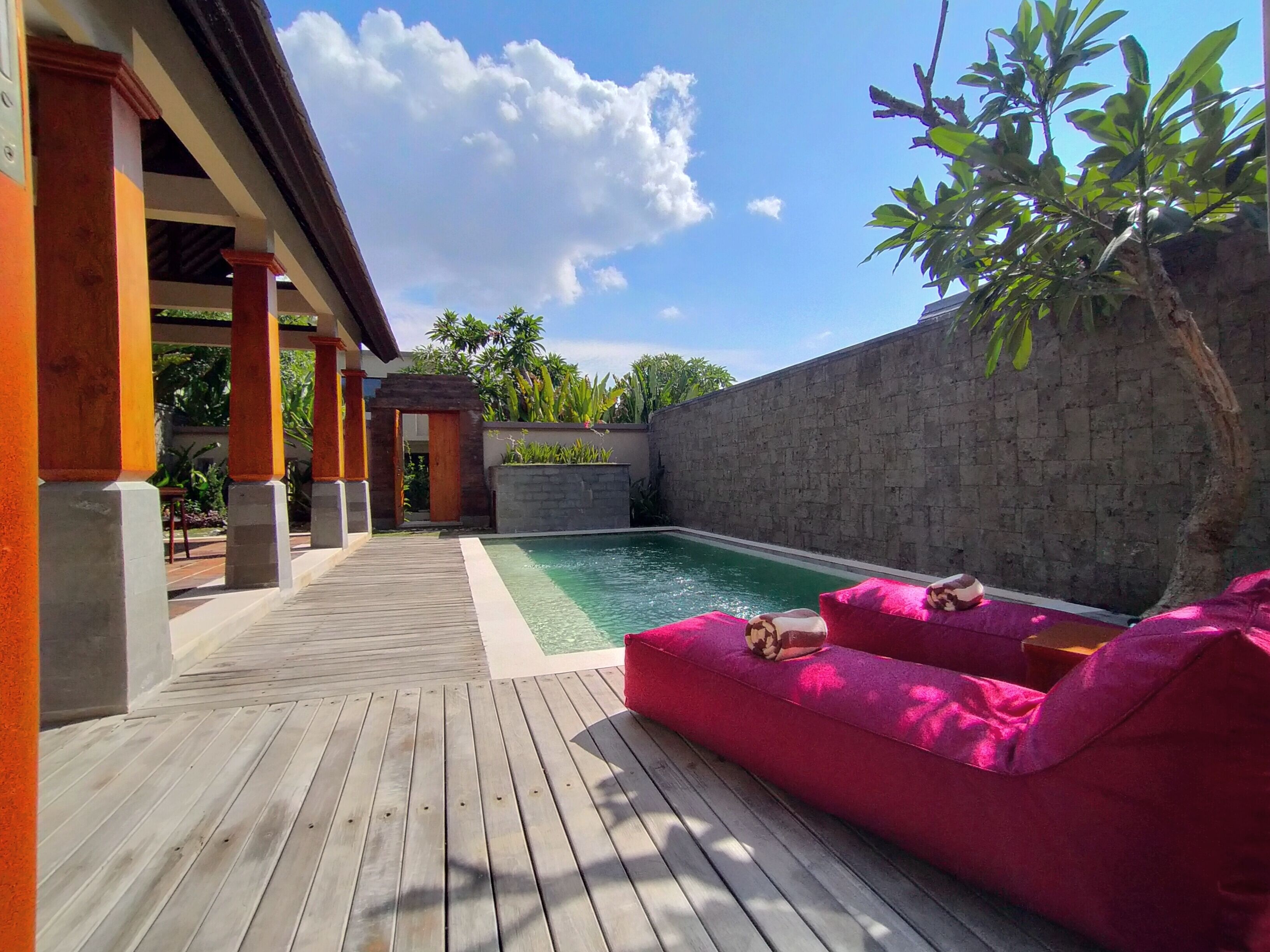 A wooden deck with a pool, a stone wall, and a pink sofa.