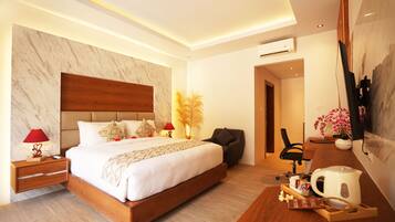 A modern hotel room with a large bed, a desk with a coffee maker, a chair, and a TV mounted on the wall.