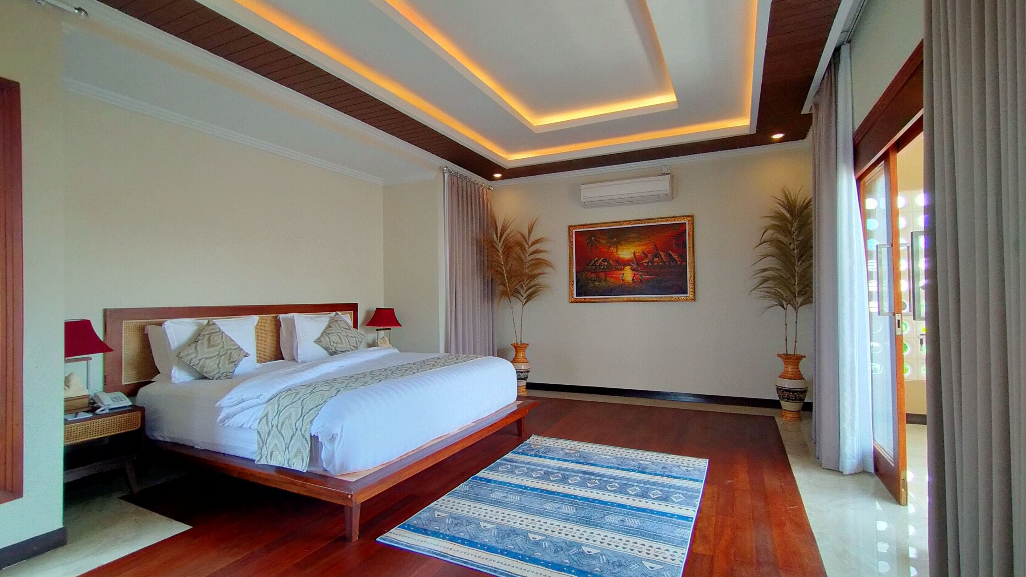 A spacious bedroom with a large bed, wooden headboard, and a patterned rug.