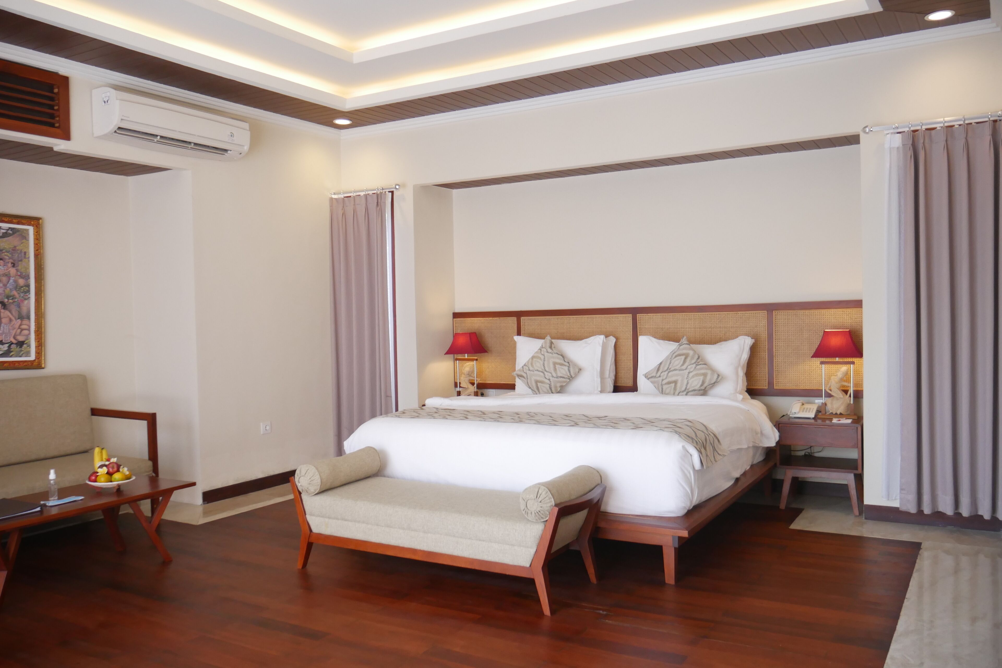 A hotel room with a large bed, two bedside tables with lamps, a sofa, and a small table with fruit.