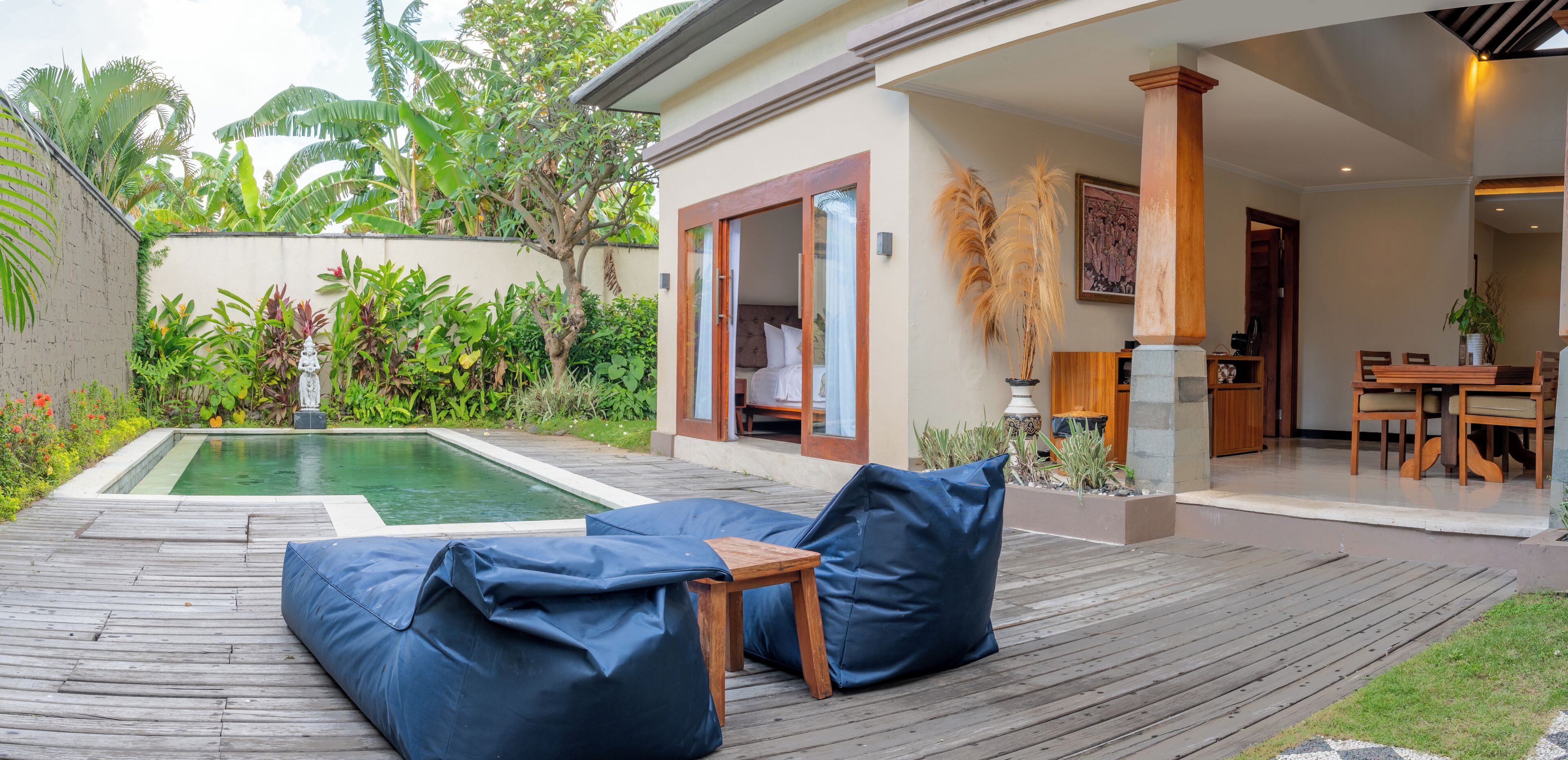 Zona junto a la piscina con terraza de madera, puffs azules y un comedor con muebles de madera.