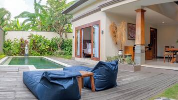 Zona junto a la piscina con terraza de madera, puffs azules y un comedor con muebles de madera.