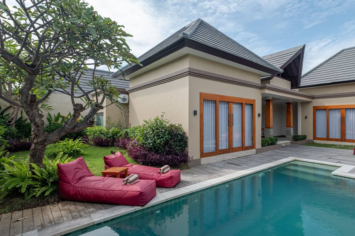 Una casa moderna con piscina, mobiliario exterior rojo y un jardín bien cuidado.