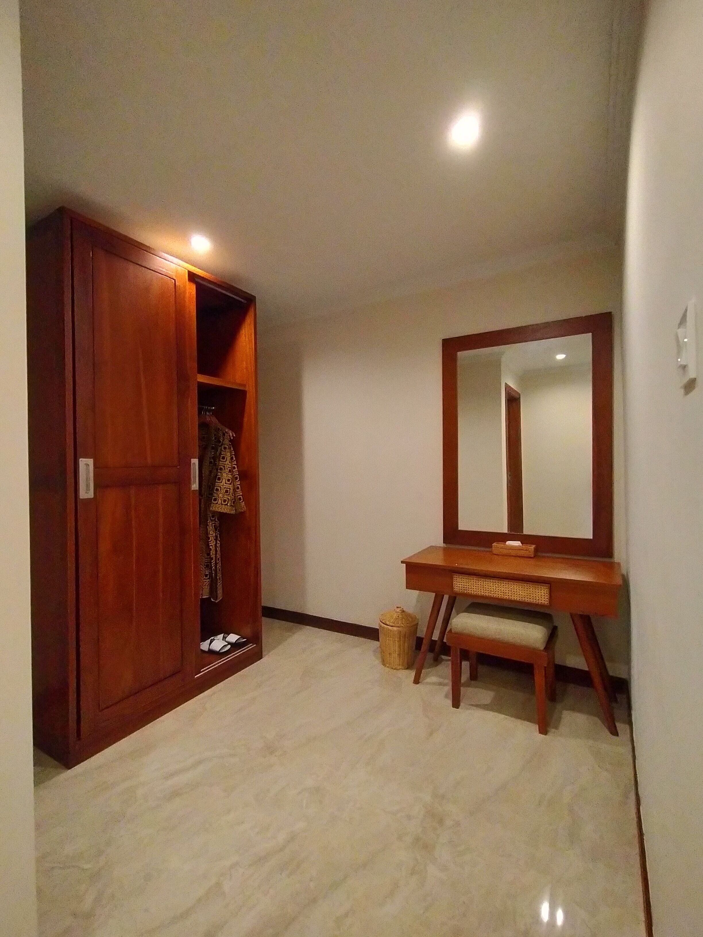 Una habitación con un armario de madera, un tocador con espejo y un pequeño banco.