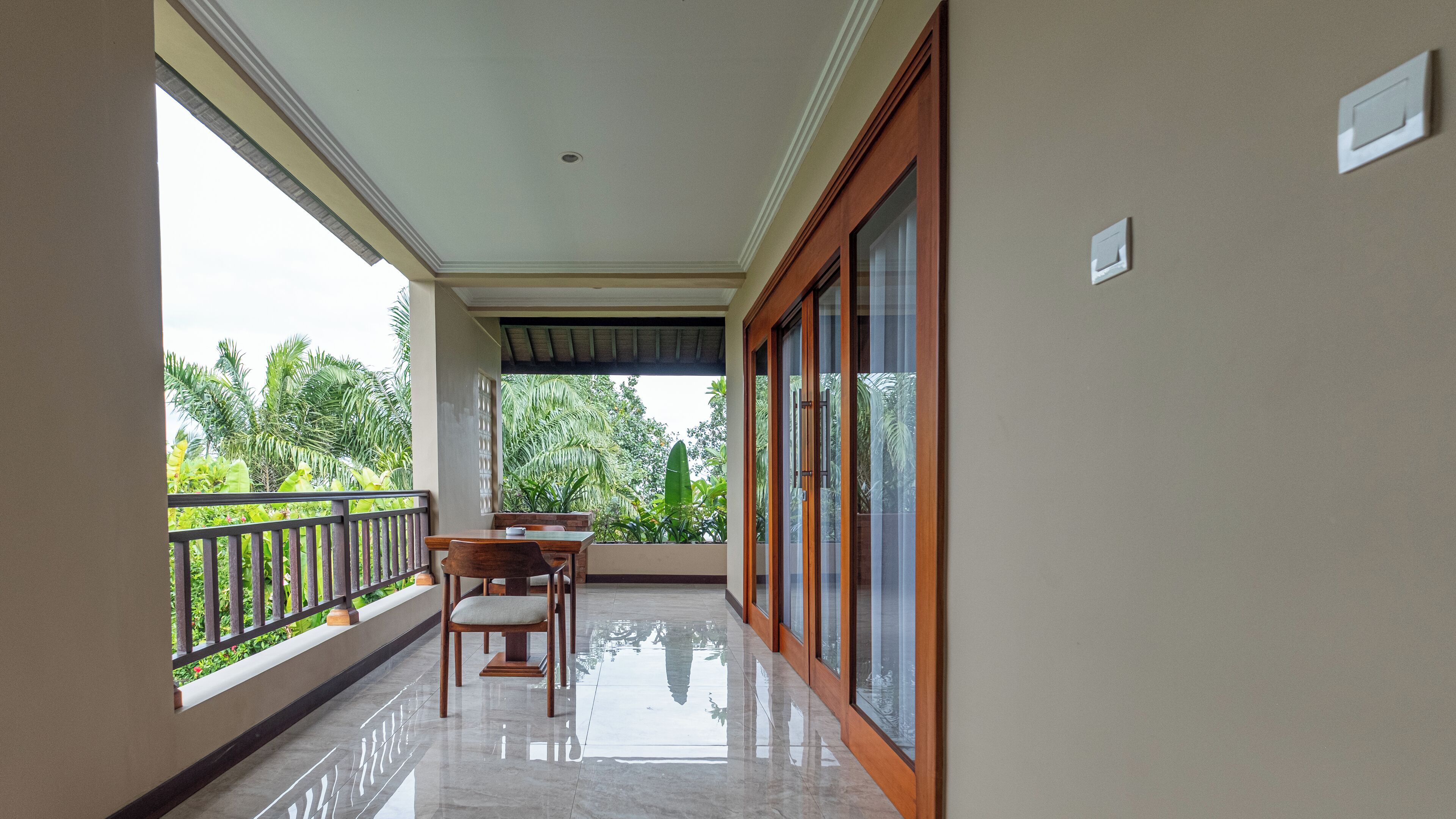 A balcony with a wooden table and chairs, a glass door, and a view of greenery.