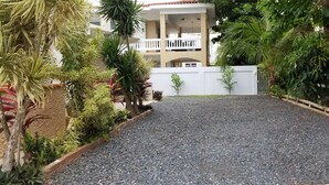 A courtyard with a gravel path, surrounded by lush greenery and a white building with balconies.
