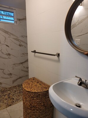 Ein Badezimmer mit Marmorwand, einem runden Spiegel, einem weißen Waschbecken und einem gewebten Hocker.