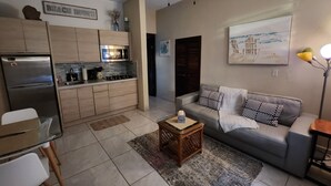 A modern living room with a grey sofa, a coffee table, and a kitchen area with wooden cabinets and a refrigerator.