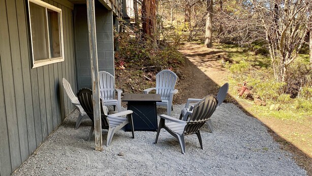 Et udendørs opholdsområde med Adirondack-stole og et bord, grusunderlag og en bygning med et vindue og en dør.