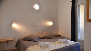 Ett sovrum med en säng, två sängbord, en vägglampa och ett fönster med gardiner.