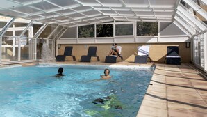 Una piscina interior con agua cristalina, techo cubierto y sillones de descanso a orillas de la piscina.