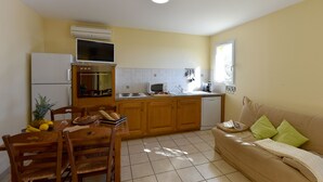 A compact kitchen with a dining area, wooden cabinets, a built-in oven, and a window providing natural light. - Villa 1 Chambre (2 - 4 Personnes) (Sainte-Lucie de Porto-Vecchio)