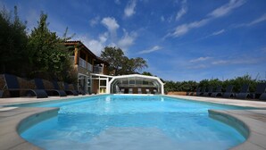 A swimming pool with a circular edge, surrounded by lounge chairs and a building with a covered area. - Villa 2 Chambres (4 Personnes) (Sainte-Lucie de Porto-Vecchio)