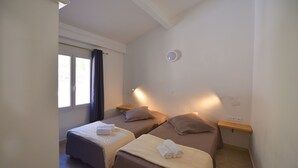 A room with two beds, a window with curtains, a wall-mounted light, and a small wooden shelf. - Villa 2 Chambres (4 - 6 Personnes) (Sainte-Lucie de Porto-Vecchio)