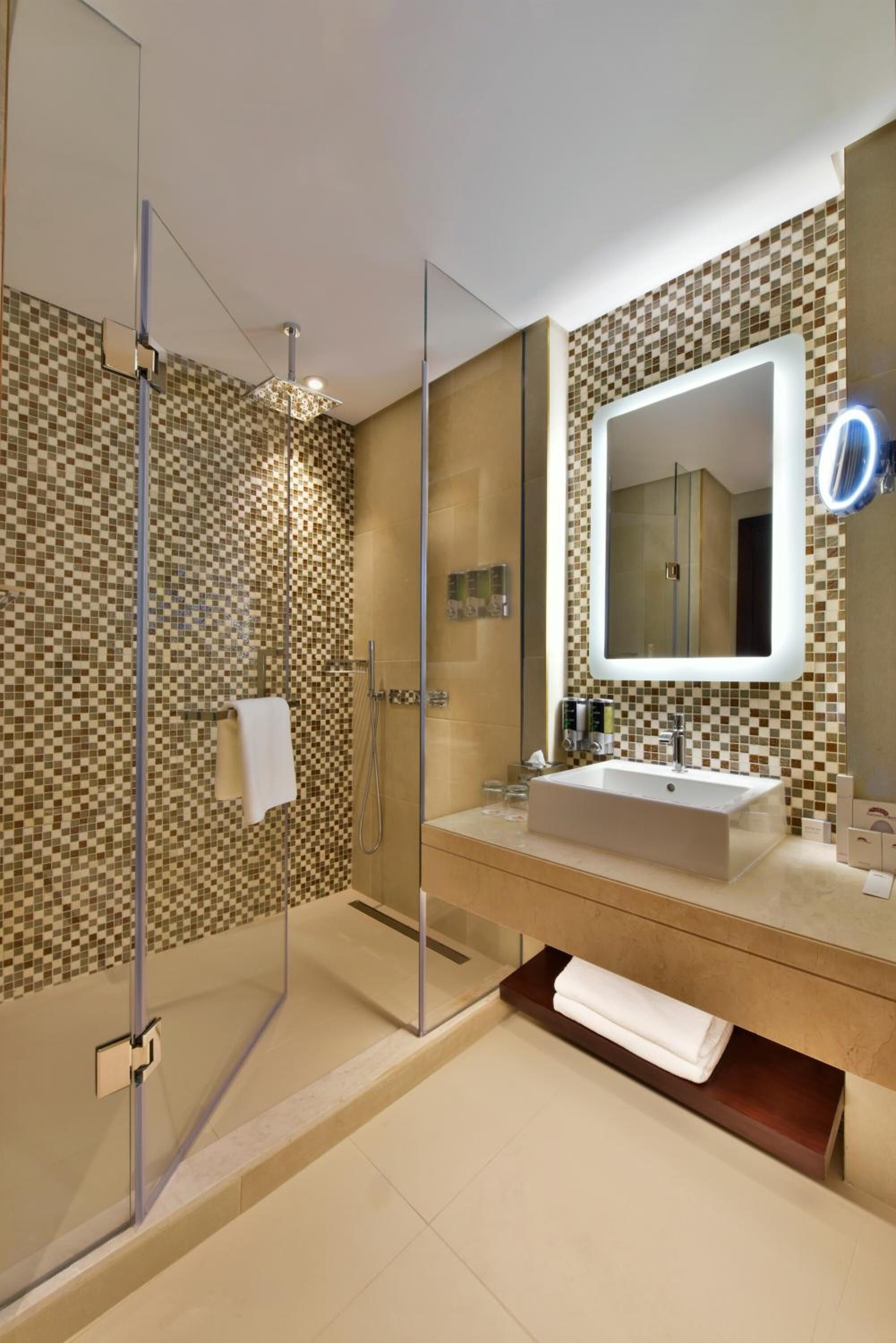 Un baño moderno con ducha de vidrio, un espejo grande y un muro con azulejos color beige.