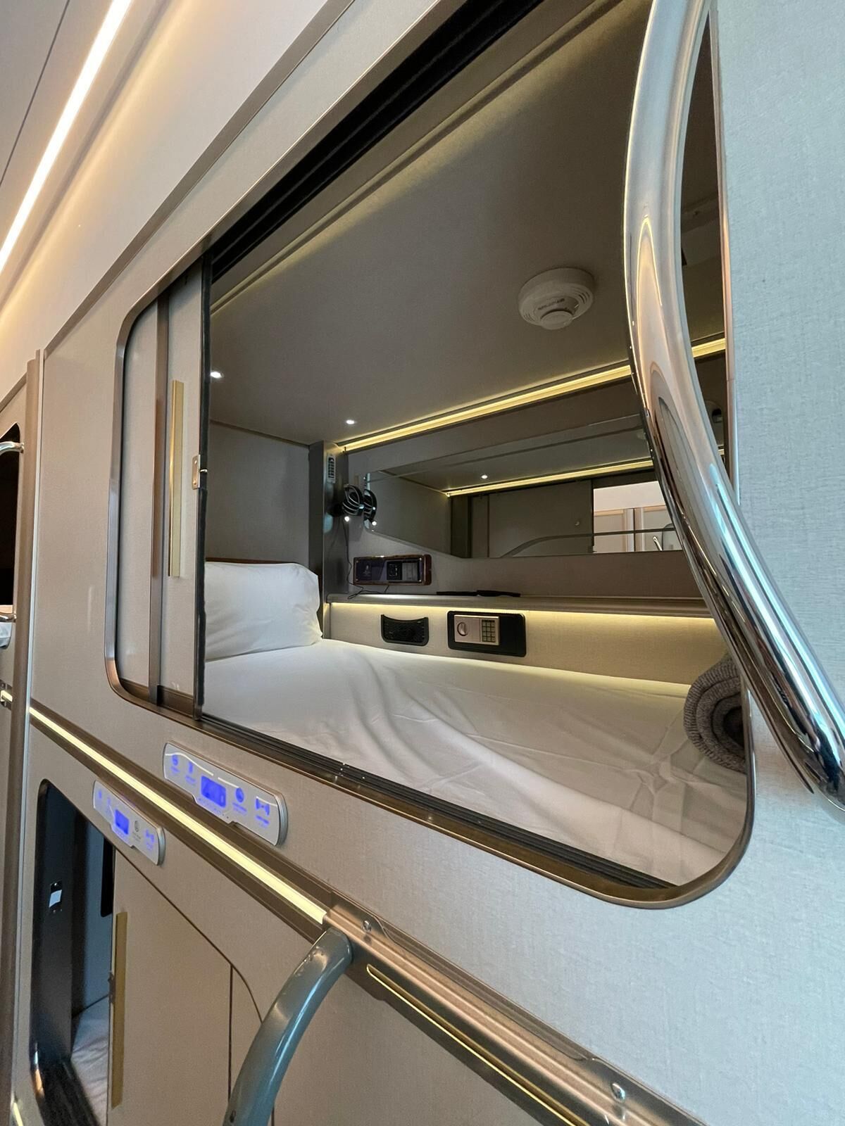 A compact, well-lit interior with a bed, control panel, and a small table.