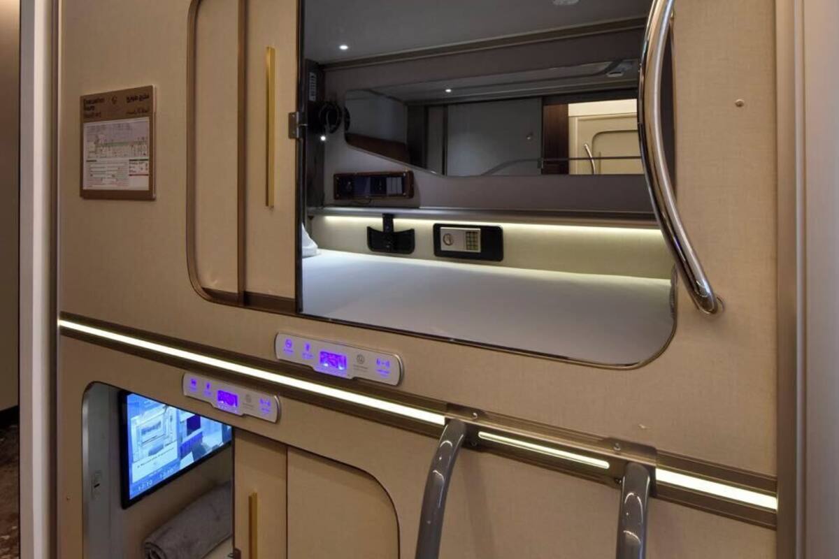 Una carrozza ferroviaria con un letto, un tavolino, un pannello di controllo e una finestra.