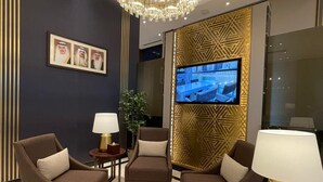 A modern living room with a large chandelier, a flat-screen TV, and a patterned wall. - Bahrain Airport Hotel Airside Hotel for Transiting and Departing Passengers only (Muharraq)