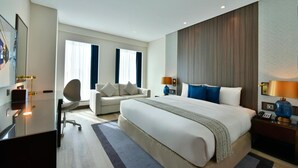 A modern hotel room with a large bed, a desk, a chair, and a sofa. - Bahrain Airport Hotel Airside Hotel for Transiting and Departing Passengers only (Muharraq)