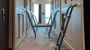 A hotel hallway with a carpeted floor, metal handrails, and a view of the sky through a window. - Bahrain Airport Hotel Airside Hotel for Transiting and Departing Passengers only (Muharraq)