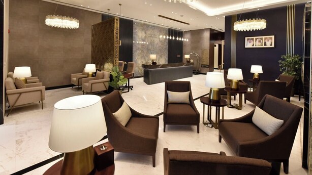 A modern lobby with a reception desk, seating area with armchairs and lamps, and decorative chandeliers. - Bahrain Airport Hotel Airside Hotel for Transiting and Departing Passengers only (Muharraq)