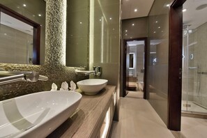 A modern bathroom with two large sinks, a textured wall, and a glass shower enclosure. - Bahrain Airport Hotel Airside Hotel for Transiting and Departing Passengers only (Muharraq)