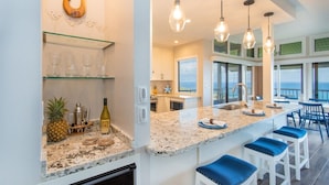 A modern kitchen with a large island, bar stools, and a view of the ocean. - Ridge 1921-22: Rare 3BR Luxury Villa w/Ocean Views (Lahaina)