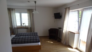 A bedroom with a bed, a chair, a TV, and a window with curtains. - Apartment Cornelia for 4 persons, 2 bedrooms, kitchenette, bathroom, 86 sqm (Inzell)