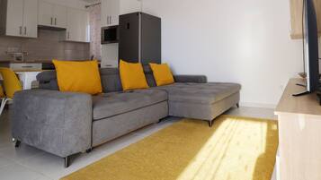 A modern living room with a grey sectional sofa, two yellow cushions, a wooden coffee table, and a yellow rug.