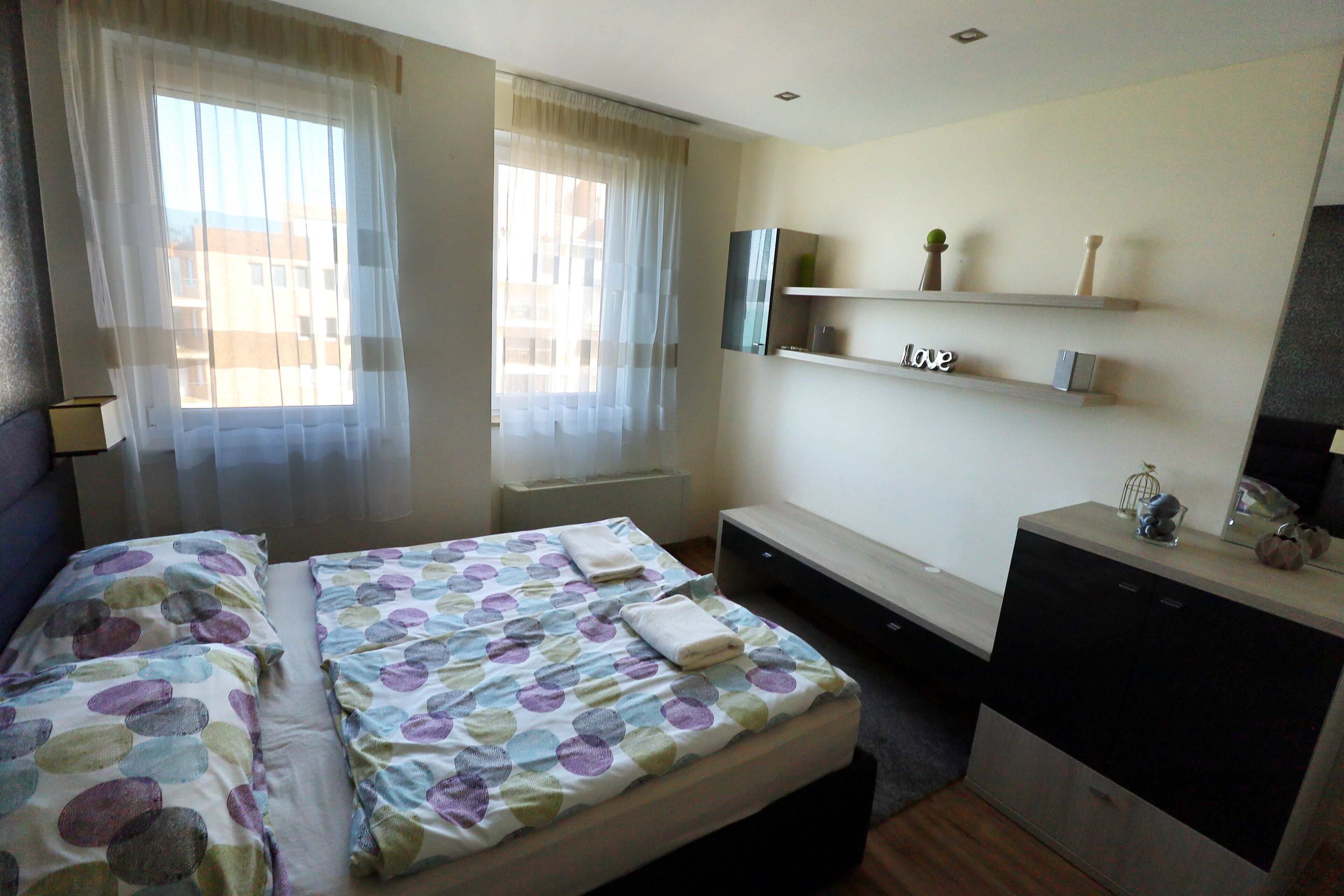 A hotel room with two beds, a desk, a mirror, and a shelf with decorative items.