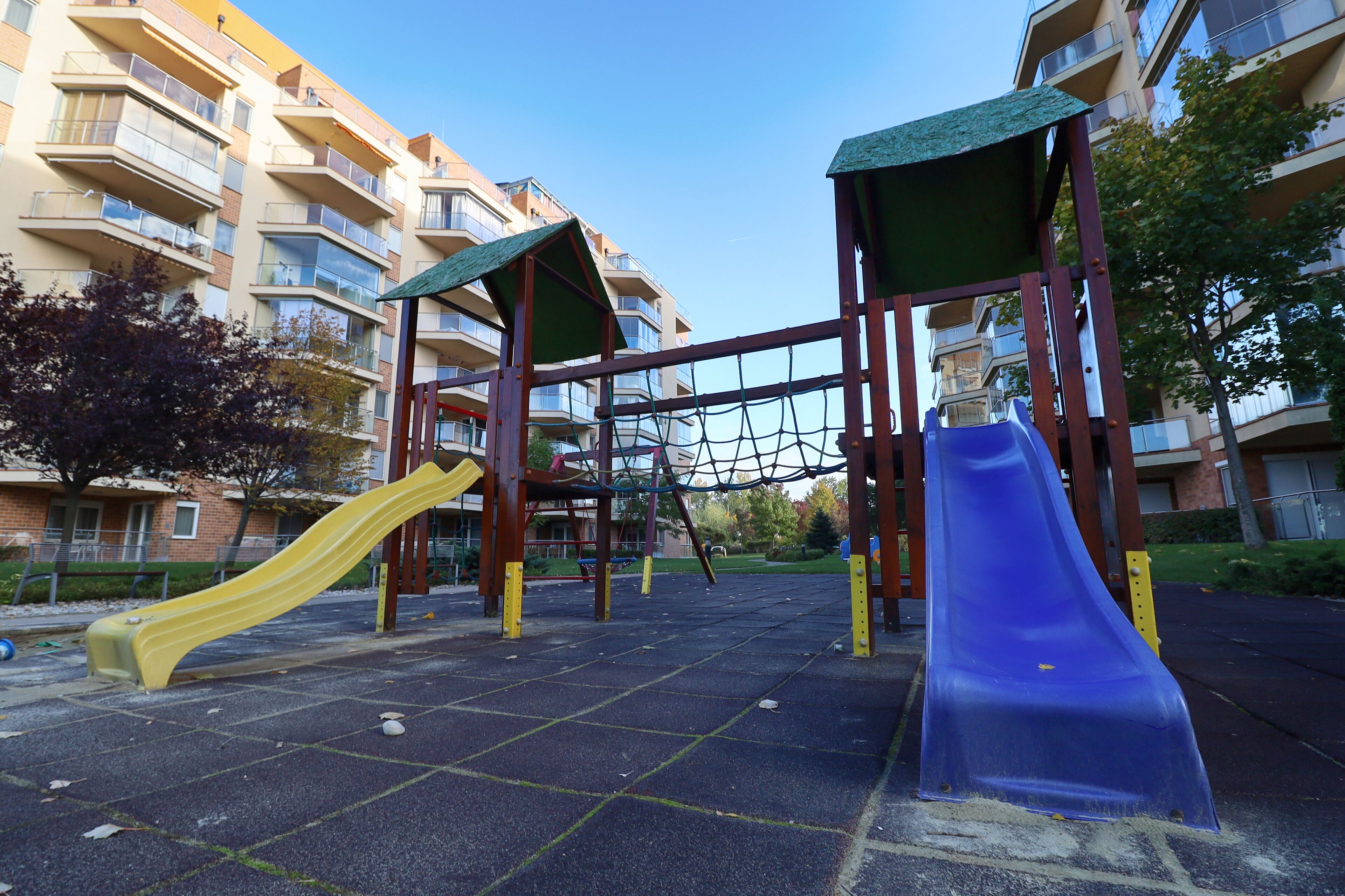 Un parc infantil amb dues tobogans i una zona de jocs de corda emmancada, tot envoltat d'edificis d'apartaments.