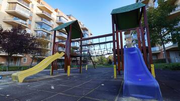 Un parc infantil amb dues tobogans i una zona de jocs de corda emmancada, tot envoltat d'edificis d'apartaments.