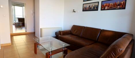 A living room with a brown leather sofa, a glass coffee table, and a cityscape wall art.