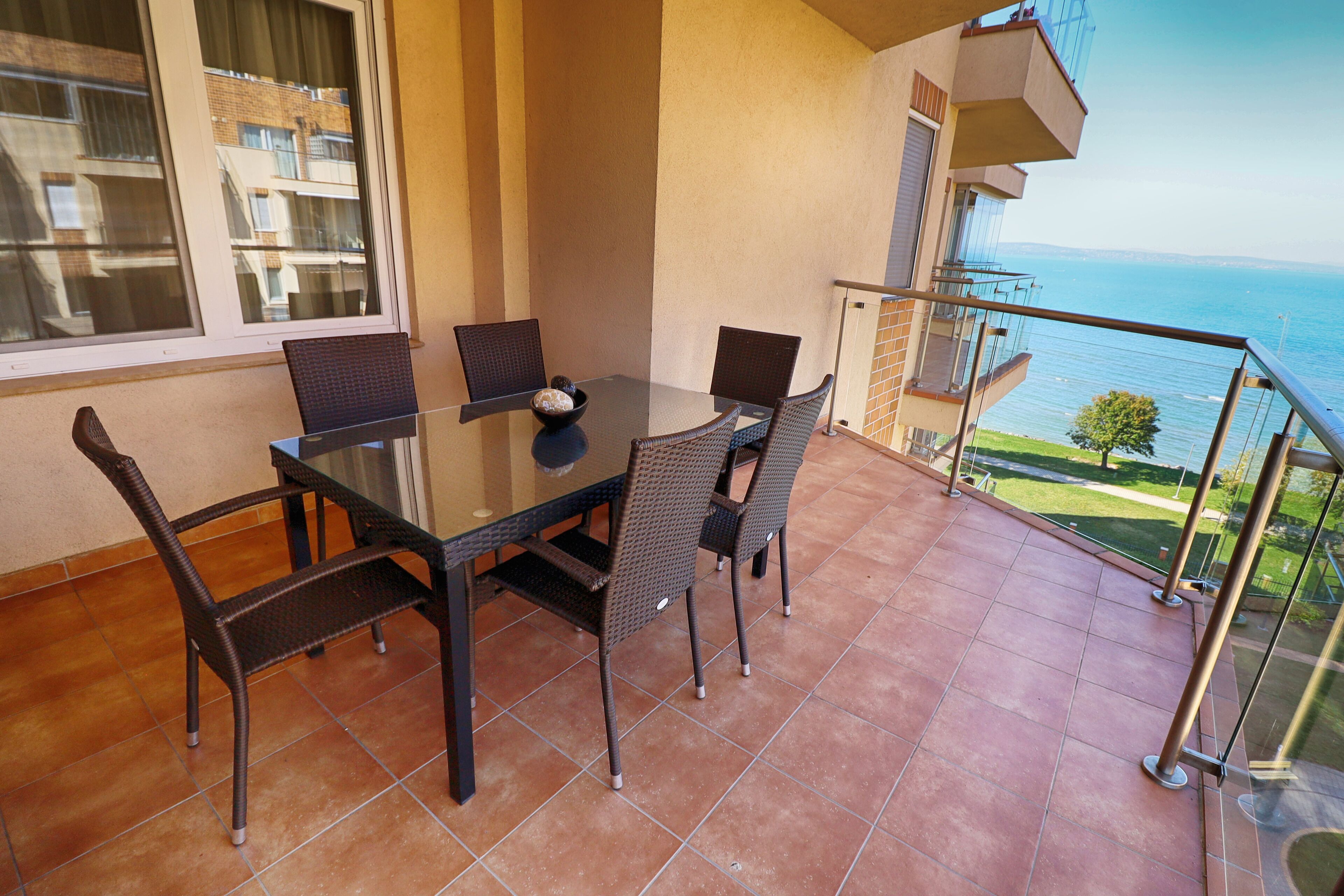 A balcony with a table and chairs, overlooking a body of water and buildings.