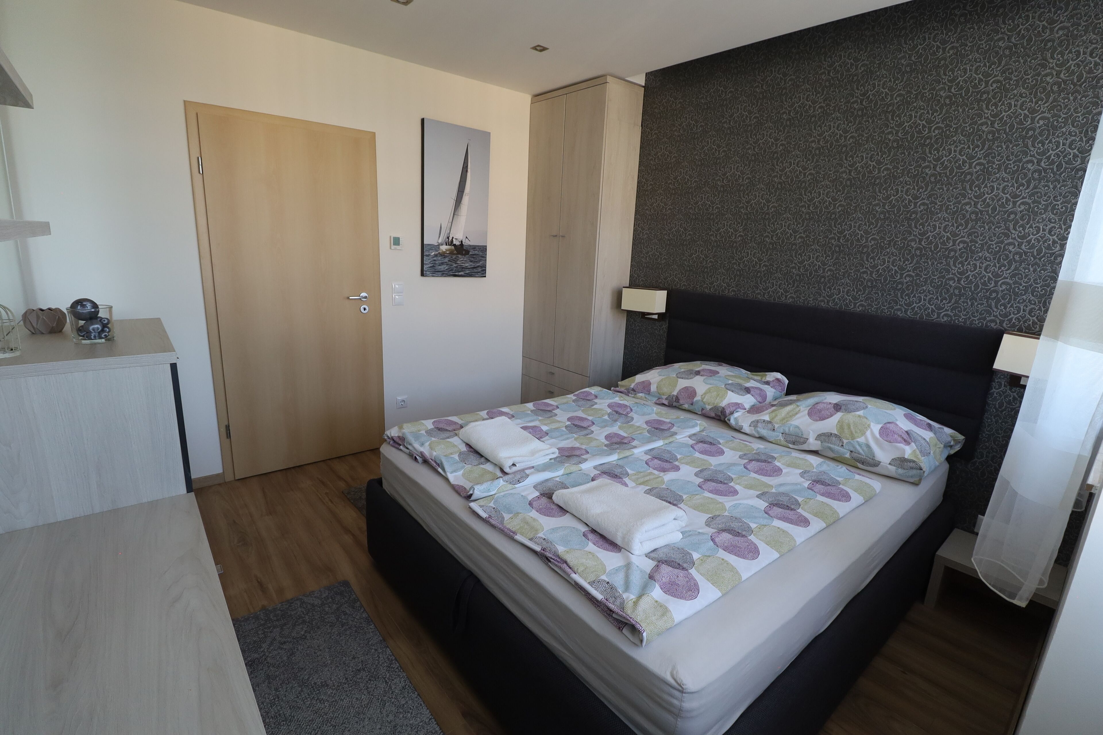 A bedroom with a bed, bedside tables, a desk, a wardrobe, and a painting on the wall.