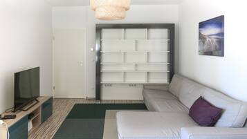 A modern living room with a sofa, a flat-screen TV, a bookshelf, and a door.