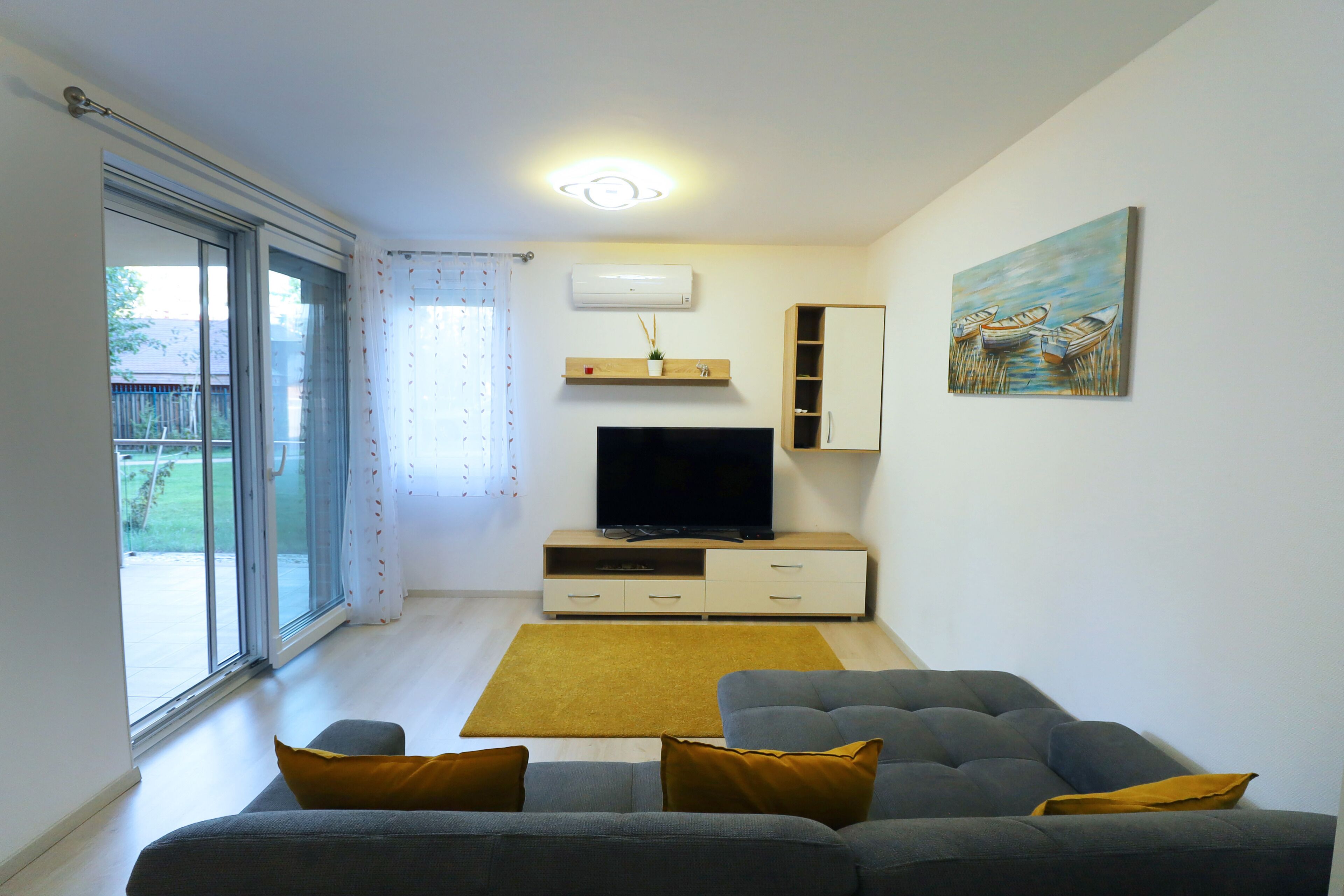 Una sala de estar con un sofá gris, un televisor de pantalla plana, un mueble de madera y un cuadro en la pared.