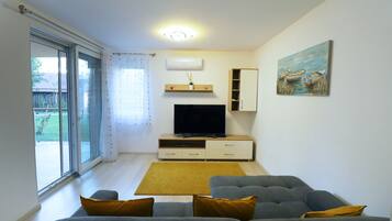 Una sala de estar con un sofá gris, un televisor de pantalla plana, un mueble de madera y un cuadro en la pared.
