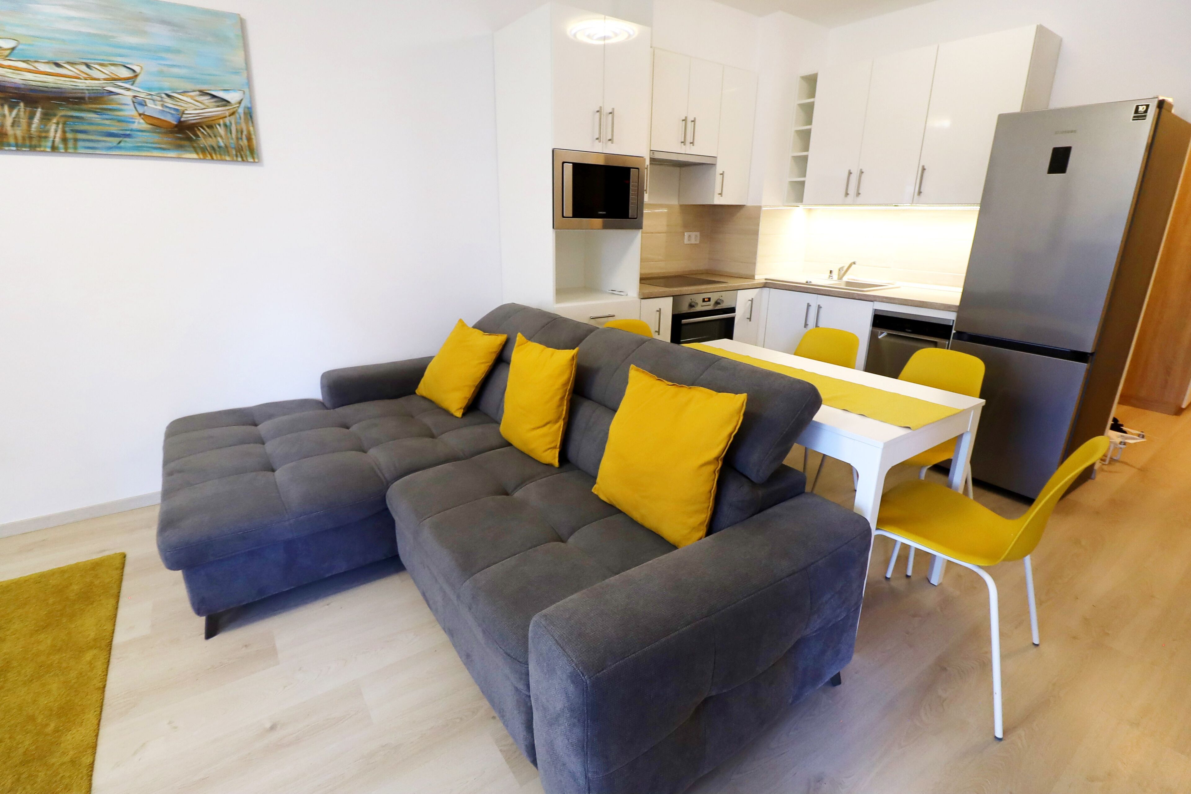 Una sala de estar moderna con un sofá seccional gris, cojines amarillos, una mesa de comedor blanca y sillas amarillas.